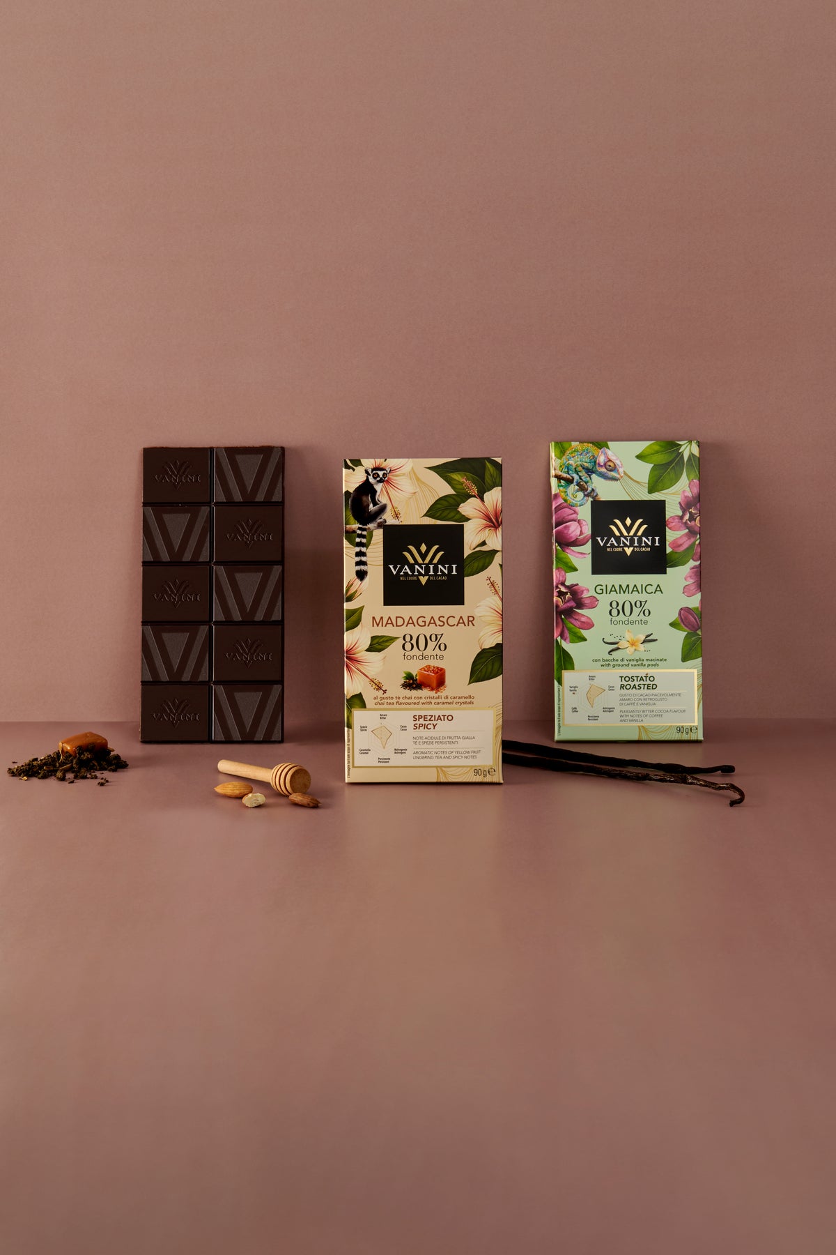 Presentazione della gamma Vanini Monorigine 80% con tavoletta di cioccolato e confezioni decorative. Gli ingredienti sul piano suggeriscono le note speziate e tostate caratteristiche delle referenze.