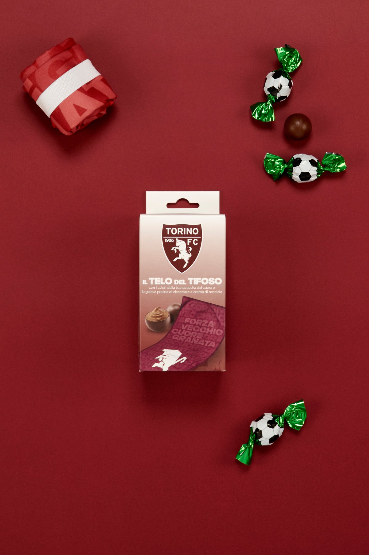 Confezione Torino FC "Il Telo del Tifoso" affiancata da praline di cioccolato incartate a tema calcio e dal telo del tifoso piegato, su elegante sfondo granata.