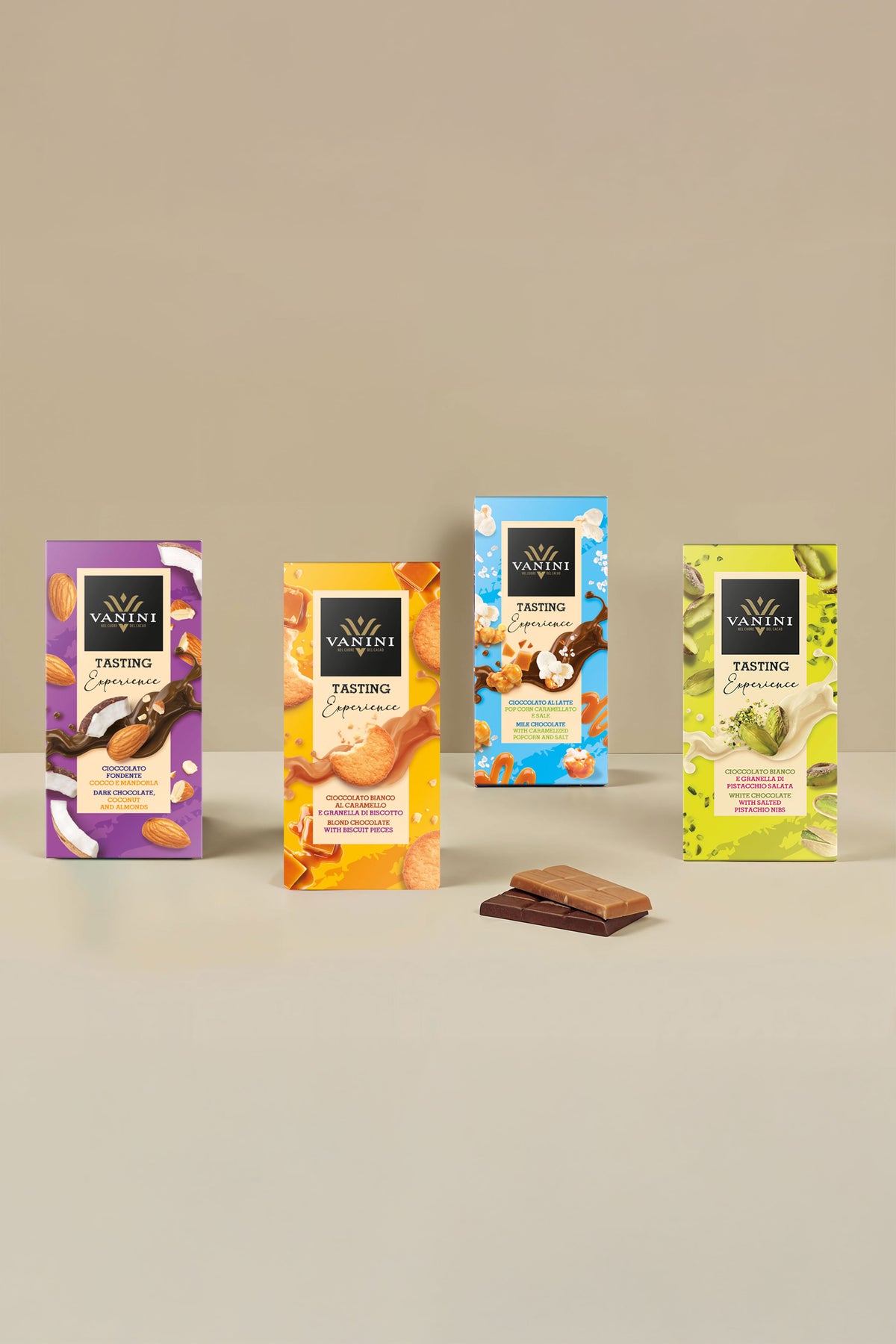 Collezione Vanini Tasting Experience composta da quattro tavolette di cioccolato assortite disposte su sfondo beige minimalista. Le referenze includono cioccolato fondente con cocco e mandorle, cioccolato bianco al caramello con granella di biscotto, cioccolato al latte con popcorn caramellati e sale e cioccolato bianco con granella di pistacchio salata. Le confezioni colorate, decorate con immagini degli ingredienti, valorizzano l'incontro tra cioccolato e inclusioni dal gusto originale.