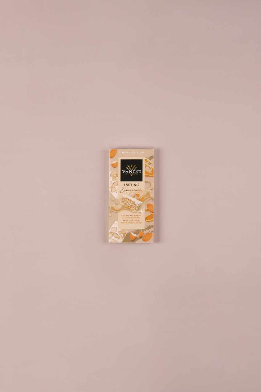 video tavoletta di cioccolato bianco al torrone si scarta e si divide, su sfondo neutro e decorato con torroni e mandorle.